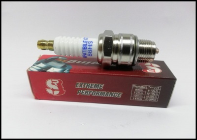 Vela de ignição branca e prata sobre caixa vermelha e preta com texto, fundo branco.