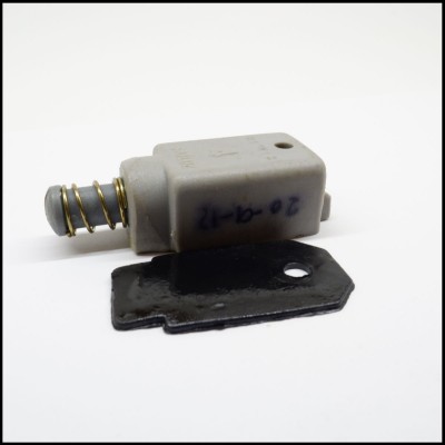 Componente mecânico cinzento com mola dourada e placa preta metálica