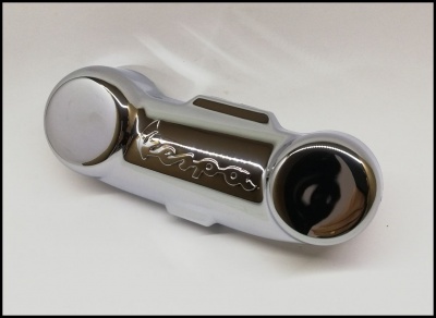 Peça metálica cromada brilhante com inscrição Vespa