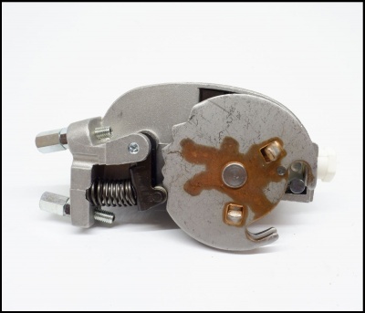 Peça metálica com mola e parafusos, com sinais de ferrugem, sobre fundo branco