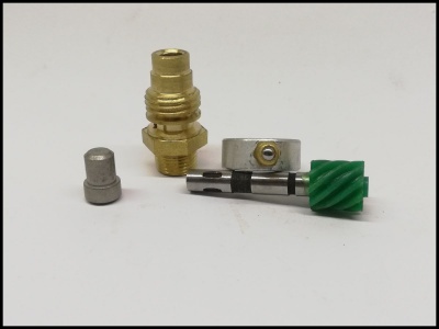 Peças metálicas pequenas incluindo uma peça dourada com rosca e engrenagem verde