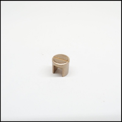 Pequena peça metálica dourada cilíndrica com ranhura no topo sobre fundo branco