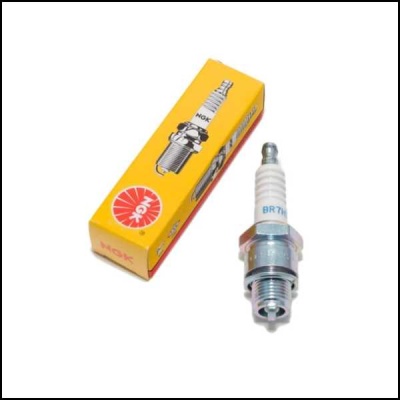 Vela de ignição NGK branca e metálica ao lado de caixa amarela NGK