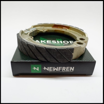 Sapata de travão Newfren com material de fricção preto e estrutura metálica dourada sobre caixa preta com logo e texto.