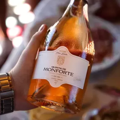 Garrafa de vinho rosé Quinta de Monforte sendo segurada com comida ao fundo