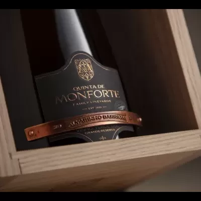 Garrafa de vinho Quinta de Monforte com rótulo preto e dourado, fita de metal cobre e caixa de madeira clara