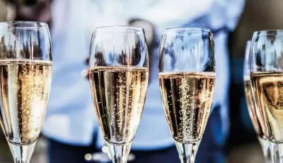 Quatro copos de champanhe com líquido dourado e bolhas, fundo desfocado com pessoa ao fundo.