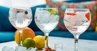 Três copos de bebida com gelo e frutas sobre mesa com frutas frescas ao lado