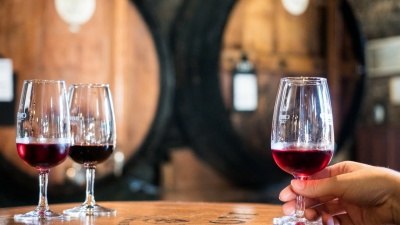 Três copos de vinho tinto com tonéis ao fundo.