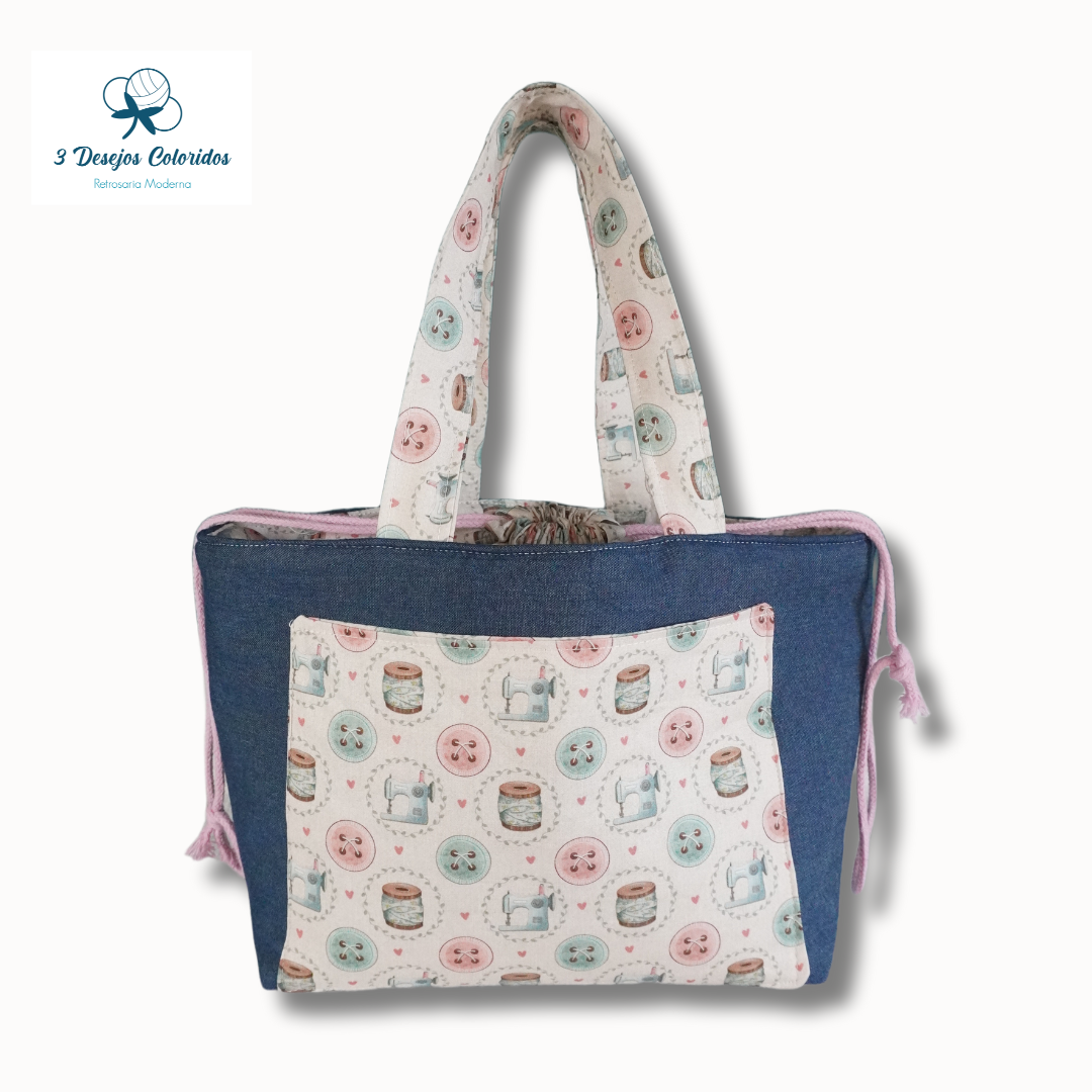 Bolsa azul-escura com bolso estampado de botões e carretéis de linha e alças com padrão similar.