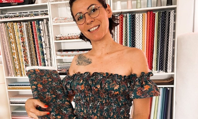 Mulher a segurar rolo de tecido floral em loja de tecidos com várias prateleiras ao fundo