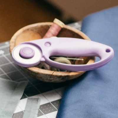 Cortador rotativo lilás sobre tabuleiro de corte com tecido e tigela de madeira