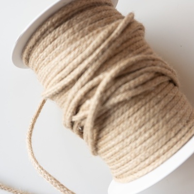 Rolo de fio bege claro num carretel branco sobre superfície branca