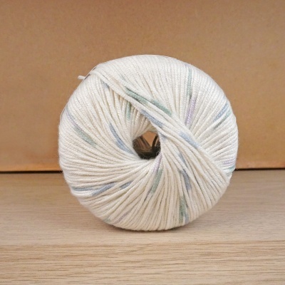 Rolo de fio branco com detalhes coloridos sobre superfície de madeira.