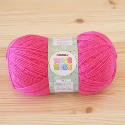 Novelo de lã cor-de-rosa com rótulo verde claro da marca Círculo sobre mesa de madeira