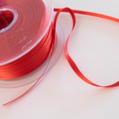 Rolo de fita vermelha fina em carretel transparente sobre fundo branco