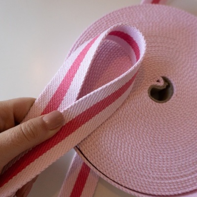 Faixa têxtil rosa com riscas vermelhas em rolo, com mão a segurá-la