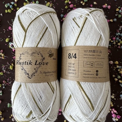 Dois novelos de fio branco com rótulos castanhos sobre superfície escura com flores coloridas