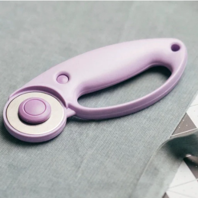 Cortador rotativo lilás sobre tecido cinzento