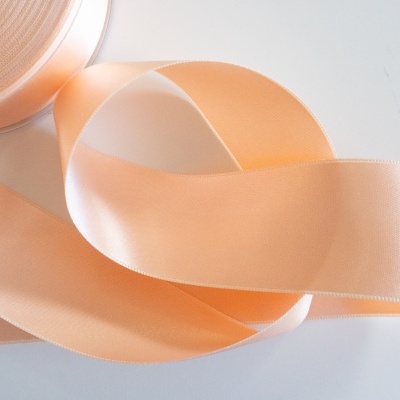 Fita de cetim pêssego suave enrolada sobre superfície branca