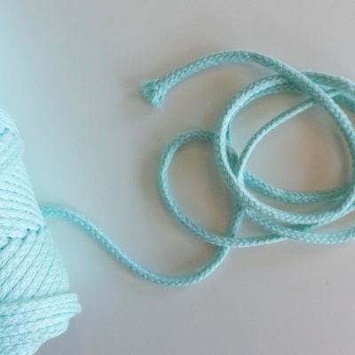 Novelo de cordão azul claro com textura trançada sobre fundo branco