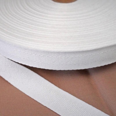 Rolo de fita têxtil branca com padrão de espinha de peixe sobre superfície castanha