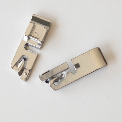 Dois pés calcadores metálicos para máquina de costura sobre fundo branco.