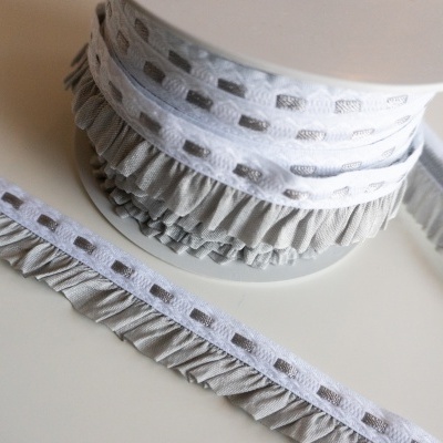 Fita branca com recortes quadrados e franjas cinzentas em rolo