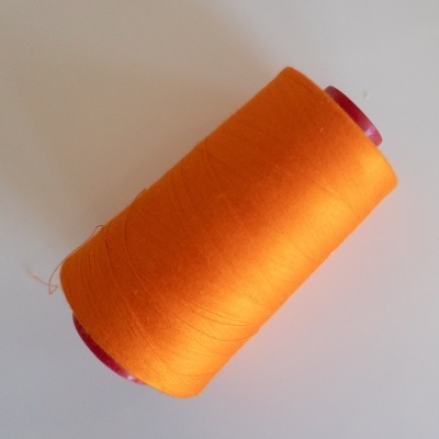 Rolo de linha laranja com carretel vermelho sobre superfície branca