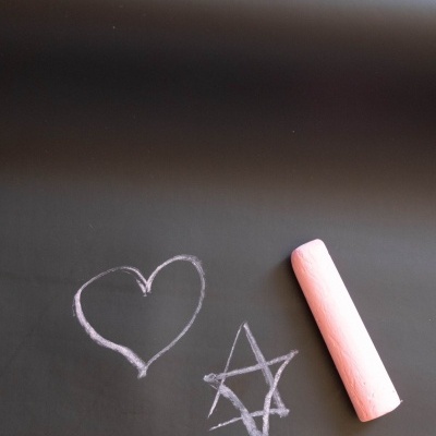 Quadro negro com desenhos de coração e estrela feitos com giz rosa e um pedaço de giz cor-de-rosa ao lado.
