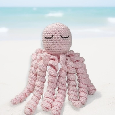 Brinquedo de croché em forma de polvo cor de rosa na areia da praia