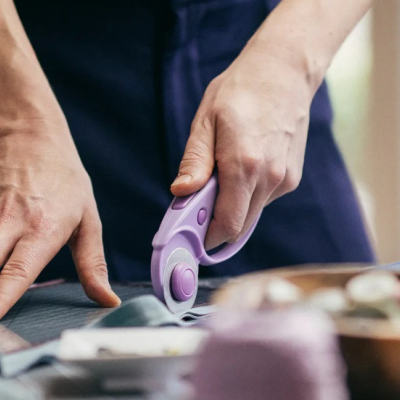 Tesoura de corte rotativo roxa cortando tecido cinzento