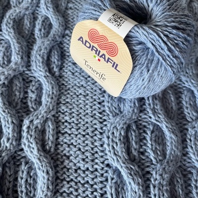 Novelo de lã Adriafil Tenerife cinzento claro sobre tecido tricotado com tranças