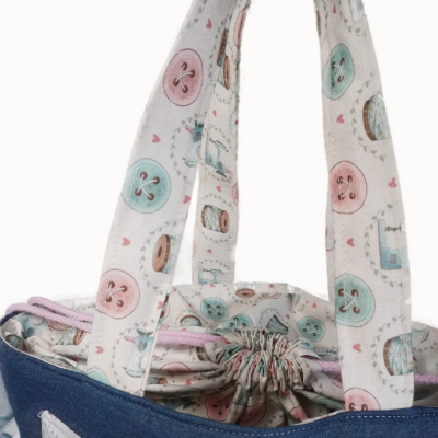 Bolsa azul com alças e interior estampados com botões e carretéis em tons pastel.