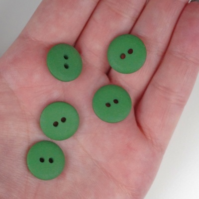 Cinco botões verdes redondos com dois buracos cada na palma de uma mão