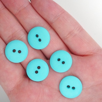 Cinco botões azuis turquesa com dois furos na palma de uma mão