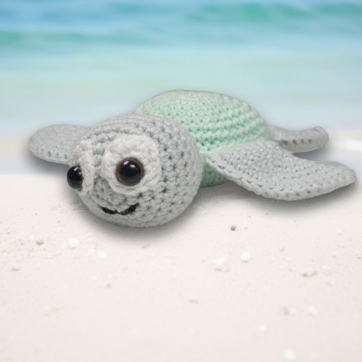 Urso-marinho de croché cinza e verde claro na praia