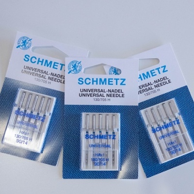 Três pacotes de agulhas de costura SCHMETZ em embalagens azuis e brancas.