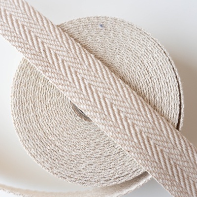Fita de tecido bege com padrão espinha de peixe enrolada em superfície branca
