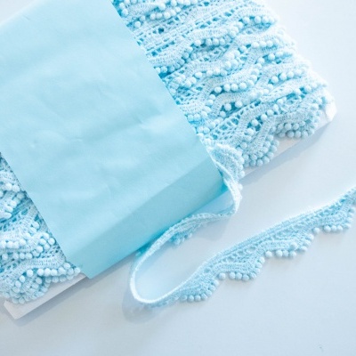 Fita de renda azul clara com pérolas enrolada em cartão branco