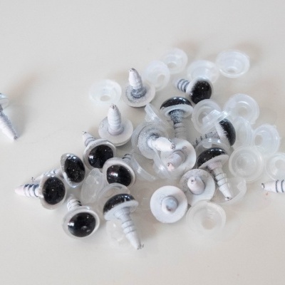 Olhos de plástico pretos com pinos brancos e arruelas transparentes sobre mesa branca