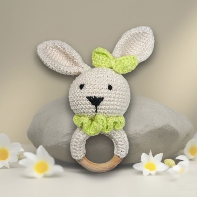 Chocalho de madeira com coelho de crochê, pedras e flores ao fundo