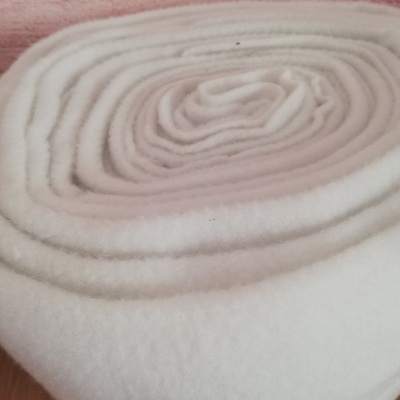 Rolo grande de tecido branco macio sobre superfície de madeira clara