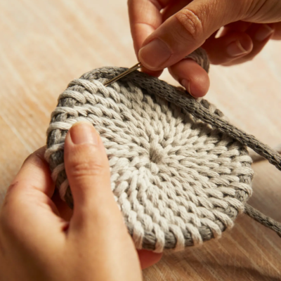 Mãos a fazer trabalho manual com fios cinzentos e agulha metálica