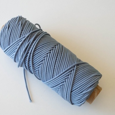 Rolo de fio azul claro num carretel de cartão sobre superfície branca