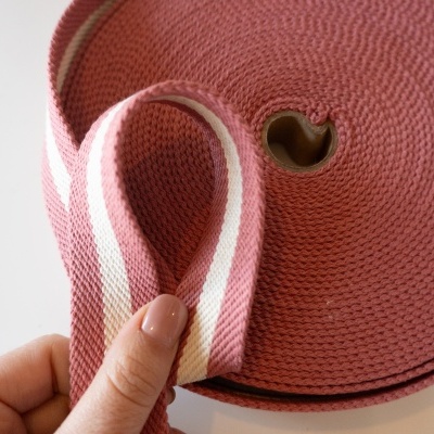 Rolo de fita têxtil rosa com riscas brancas e mão segurando a fita