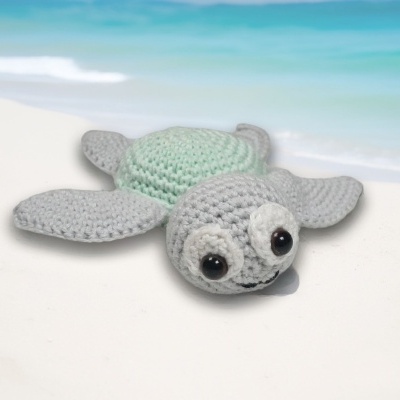 Tartaruga de croché cinzenta e verde claro junto à praia