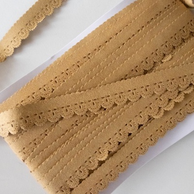 Fita decorativa bege em padrão rendado enrolada numa superfície branca