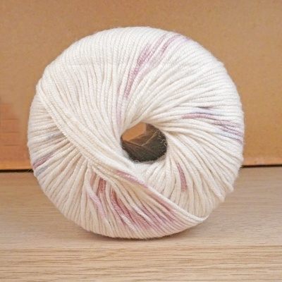 Novelo de lã branca com manchas rosa numa superfície de madeira clara