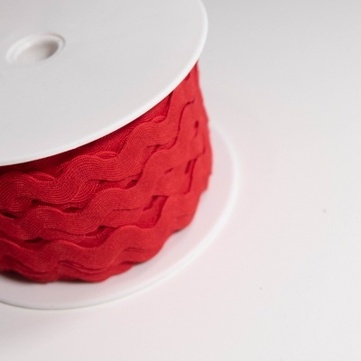 Carretel de fita decorativa vermelha com padrão ondulado num suporte branco